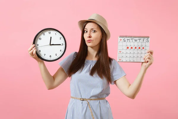 Shocked confused sad woman in blue dress holding round clock, periods calendar for checking menstruation days isolated on trending pink background. Medical gynecological concept. Copy space
