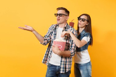 Genç tahriş çift kadın adam 3d gözlük tarihte film film izlerken kova patlamış mısır fincan izole sarı arka plan üzerinde patlamış mısır çalmak kola veya kola işaret eden bir ele tutun. Duygu sinema