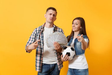 Genç kazanmak çift, kadın erkek, dolar, nakit para, futbol topu, paket tutan futbol taraftarları destek ekibi üzerinde sarı arka plan izole neşelen. Spor bahis heyecan şevk aile yaşam tarzı kavramı