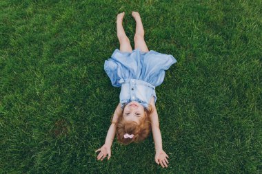 Küçük şirin çocuk bebek kız kot elbise yalan yeşil çim çim üzerinde gülümseyen, ellerini yukarı parkta kaldır. Anne, küçük çocuk kızı. Anneler günü, aşk aile, ebeveynlik, çocukluk kavramı