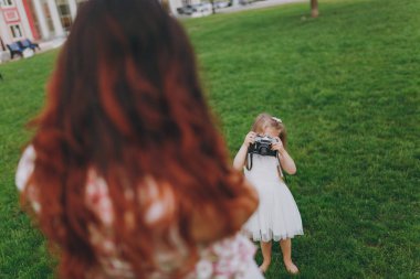 Işık elbiseli küçük çocuk bebek kız parkta yeşil çimenlerin üzerinde retro vintage fotoğraf makinesinde anne resmini al. Anne, küçük çocuk kızı. Anneler günü, aşk aile, ebeveynlik, çocukluk kavramı