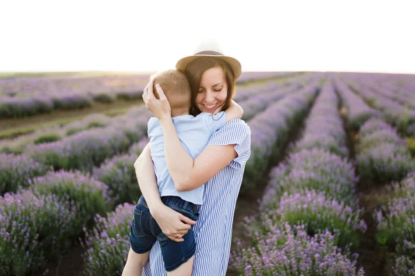 青いドレス帽子紫ラベンダー花草原フィールド背景 歩きながら若い女性楽しく かわいい子の小さな男の子と遊ぶ 母の小さな子供の息子 家族の日 子供たちのコンセプト — ストック写真