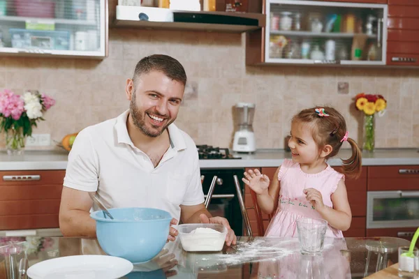 Little kid girl helps man to cook Christmas ginger cookies, plays with flour at table. Happy family dad, child daughter cooking food in weekend morning. Father's day holiday. Parenthood, childhood