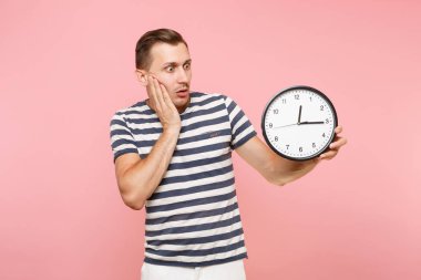 Dikey şok üzgün üzgün giyen çizgili tişört yuvarlak saat tutan adam, pastel pembe arka plan eğilimleri izole alanı kopyalayın. İnsanlar samimi duygular yaşam tarzı kavramı. Zaman azalıyor