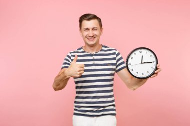 Çizgili tişört gösteren başparmak yukarıya, saat, kopya alanı tutan gülümseyen adam portresi pastel pembe arka plan eğilimleri izole. İnsanlar samimi duygular yaşam tarzı kavramı. Zaman