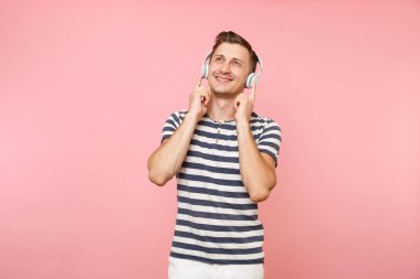 Genç adam beyaz kablosuz kulaklık ile müzik dinlemek çizgili tişört giyen gülümseyen portresi izole üzerinde gidişli pastel pembe arka plan tadını çıkarın. İnsanlar samimi duygular yaşam tarzı kavramı