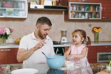 Küçük çocuk kız adam Noel zencefilli kurabiye yemek, un masasında kaseye dökün için yardımcı olur. Mutlu aile baba, hafta sonu sabah yemek yemek çocuk kızı. Babalar günü tatil. Ebeveynlik çocukluk