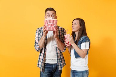 Genç sürpriz çift kadın adam rahat kıyafetler yüz kova patlamış mısır ile kapsayan tarihte film film izlerken içinde plastik bardak kola veya kola izole sarı arka plan üzerinde tutun. Sinema duygular