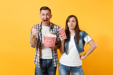 Genç kadın çift ve kova patlamış mısır ve kola plastik bardak tutan tarihte film film izleyen adamım hayret ya da başparmak gösterilen cola sarı arka plan üzerinde izole. Sinema kavramı duygular