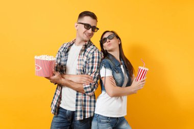 Genç mutlu çift kadın ve erkekte 3d gözlük film film izlerken patlamış mısır plastik bardak soda veya el ele tutuşarak cola kova tutarak tarihte üzerinde izole sarı arka plana katlanmış. Sinema duygular