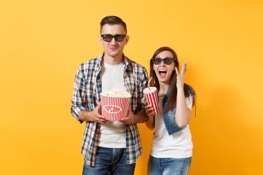Genç komik çift kadın adam 3d gözlük tutan kova patlamış mısır plastik bardak soda veya eller üzerinde sarı arka plan izole yayılan cola tarihi film film izlerken. Sinema kavramı duygular