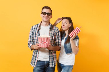 Genç çift kadın ve erkekte 3d gözlük kova patlamış mısır ve kola veya kola sarı arka plan üzerinde izole plastik bardak tutan tarihi film film izlerken gülümsüyor. Sinema kavramı duygular