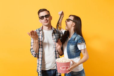 Genç komik çift kadın adam 3d gözlük yapma Klaket ve kova patlamış mısır üzerinde sarı arka plan izole klasik kara film tutan tarihi film film izlerken. Sinema kavramı duygular