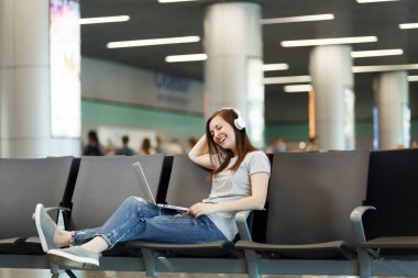 Genç neşeli gezgin turist kadın dizüstü bilgisayarda çalışan müzik dinlerken kulaklık ile Uluslararası Havaalanı'nda lobi salonunda bekleyin. Hafta sonu kaçamağı yurt dışında seyahat yolcu. Hava uçuş kavramı