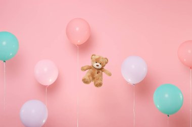 Oyuncak ayı peluş oyuncak pastel parlak gidişli pembe arka plan üzerinde renkli hava balonları ile. Dekorasyon doğum günü tatil partisi konsepti için