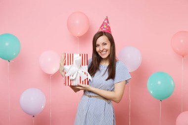 Doğum günü şapka mavi elbiseli kırmızı kutu hediye present pastel pembe renkli hava baloons ile tutarak gülümseyen çekici kadın portresi. Doğum günü tatil partisi, insanlar samimi duygular