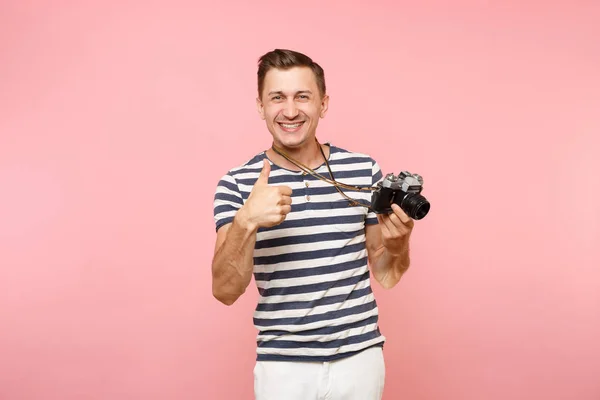 Portrait of smiling young photographer man wearing striped t-shirt take pictures on retro vintage photo camera isolated on trending pastel pink background. People sincere emotions lifestyle concept