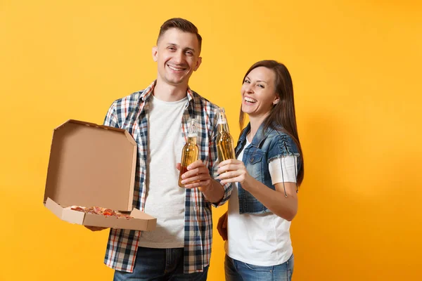 Young happy smiling couple woman and man sport fan cheer up support team hold beer bottles and italian pizza in cardboard flatbox isolated on yellow background. Sport family leisure lifestyle concept