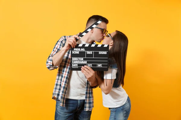 Genç mutlu güzel çift kadın adam 3d gözlük Klaket yapma ve üzerinde izole sarı arka plana öpüşme klasik kara film tutan tarihte film film izlerken. Sinema kavramı duygular