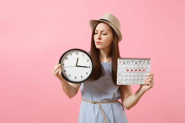 Shocked confused sad woman in blue dress holding round clock, periods calendar for checking menstruation days isolated on trending pink background. Medical gynecological concept. Copy space