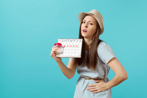 Портрет грустной женщины в платье с белой бутылкой с таблетками, календарь женских менструаций, проверка дней менструации изолированы на синем фоне. Медицинское обслуживание, гинекологическая концепция. Копирование пространства

