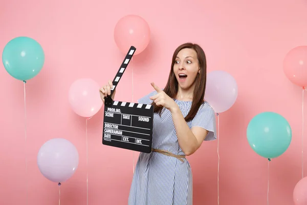 惊讶的女人的肖像 指着食指一边持有经典的黑色电影制作 Clapperboard 在粉红色的背景与五颜六色的空气 Baloons 生日聚会 人们真挚的感情 — 图库照片