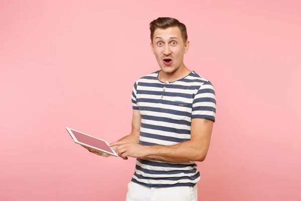 Portrait of user young man wearing striped t-shirt working on tablet pc computer isolated on trending pastel pink background. People sincere emotions lifestyle concept. Advertising area on copy space