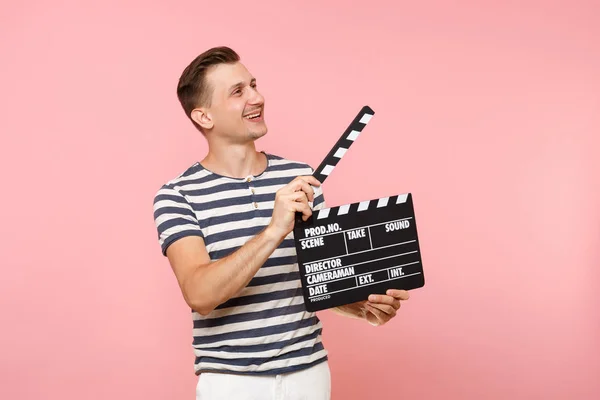 トレンドのパステル ピンクの背景に分離されたカチンコを作る古典的な黒いフィルムを保持ストライプの シャツを着て青年の肖像画 の心から感情ライフ スタイルのコンセプト 広告エリア — ストック写真