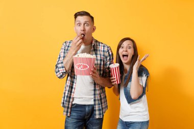 Film filmde plastik bardak kola veya kola yayılan el tutan kova patlamış mısır yemek tarihi izleyen genç şok hayran çift kadın adamım sarı arka plan üzerinde izole. Sinema kavramı duygular.