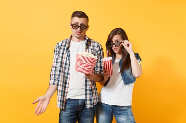 Genç çift kadın adam 3d gözlük tutan eller üzerinde sarı arka plan izole kova patlamış mısır plastik kap kola veya kola yayılan tarihi film film izlerken rahatsız edilmiş. Sinema kavramı duygular