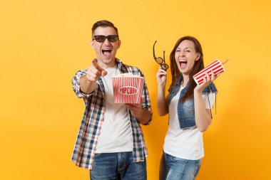 3d gözlük tarihte film film izlerken kaç kadın adam gülüyor genç kova patlamış mısır plastik bardak kola veya kola işaret parmağı üzerinde sarı arka plan izole kamera tutun. Sinema duygular