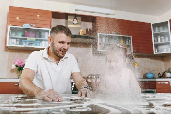 Little kid girl helps man to cook Christmas ginger cookies, sprinkling flour in kitchen at table. Happy family dad, child daughter cooking food in weekend. Father\'s day holiday. Parenthood, childhood