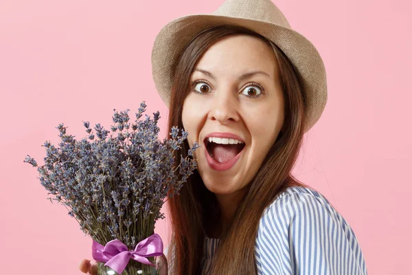 Portrait of a happy young tender woman in blue dress, hat holding bouquet of beautiful purple lavender flowers isolated on bright trending pink background. International Women\'s Day holiday concept