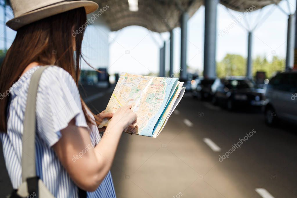 Cropped Young traveler tourist woman in hat with backpack searching route in paper map at international airport. Female passenger traveling abroad to travel on weekends getaway. Air flight concept