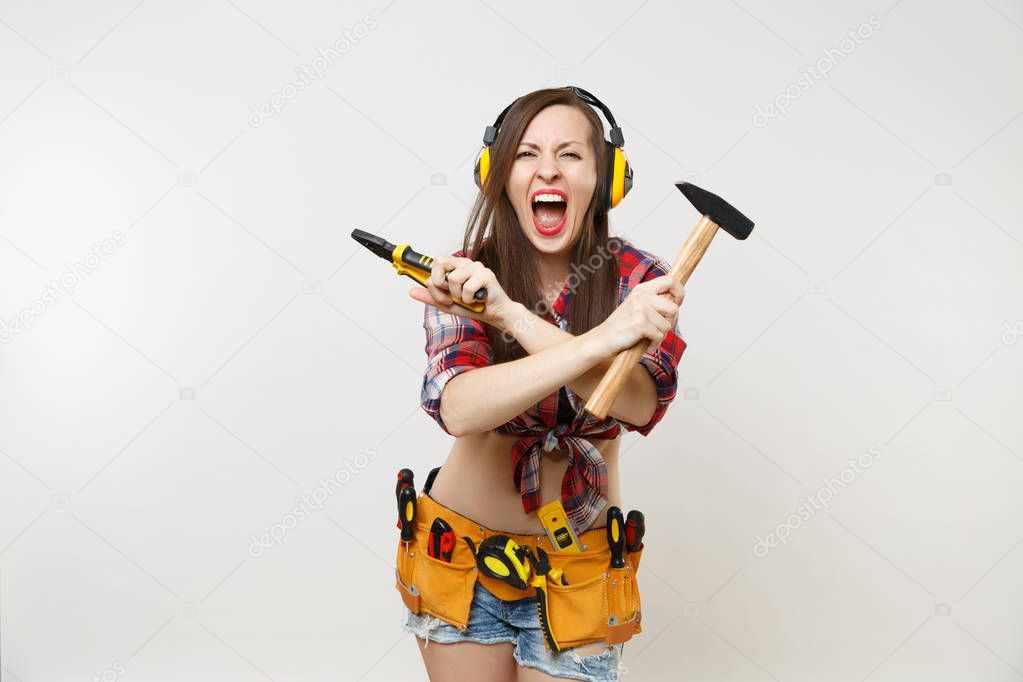Angry emotional woman in tartan shirt, denim shorts, noise insulated headphones, kit tools belt full of instruments isolated on white background. Female in male work. Renovation occupation concept