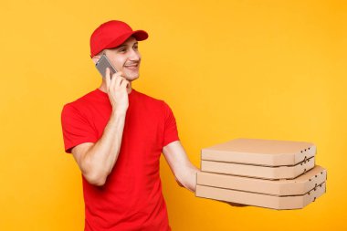 Kırmızı bere t-shirt veren yemek sipariş İtalyan pizza sarı arka plan boş boş flatbox kutularındaki teslimat adam. Erkek çalışan pizzaman kurye Mobil cep telefonu mockup üzerinde konuşuyor. Hizmet anlayışı