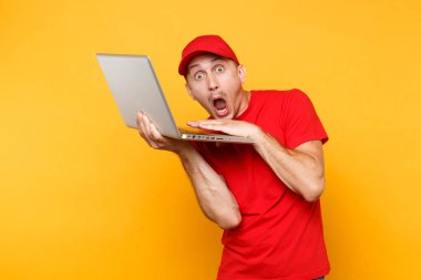 Sarı turuncu arka plan üzerinde izole teslimatçı. Profesyonel erkek çalışan kurye kırmızı şapkalı, dizüstü pc bilgisayarda yazarak çalışma tutan t-shirt. Hizmet anlayışı. Kopya alanı reklam için