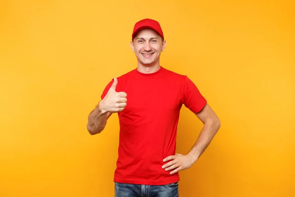 黄色オレンジ色の背景に分離の赤いユニフォームで配達人 キャップで男性従業員を笑顔の専門家 宅配便またはディーラーの表示として働いている シャツは親指ジェスチャー サービスのコンセプト — ストック写真
