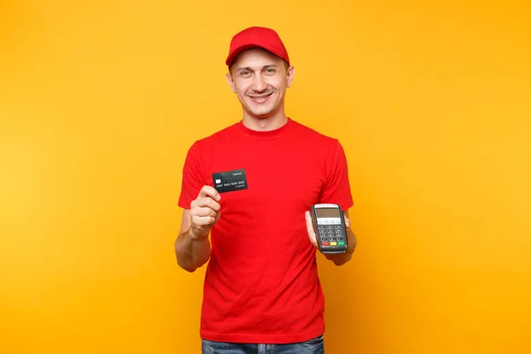 Delivery man in red uniform isolated on yellow background. Male employee in cap, t-shirt courier holding wireless modern bank payment terminal to process and acquire credit card payments, black card