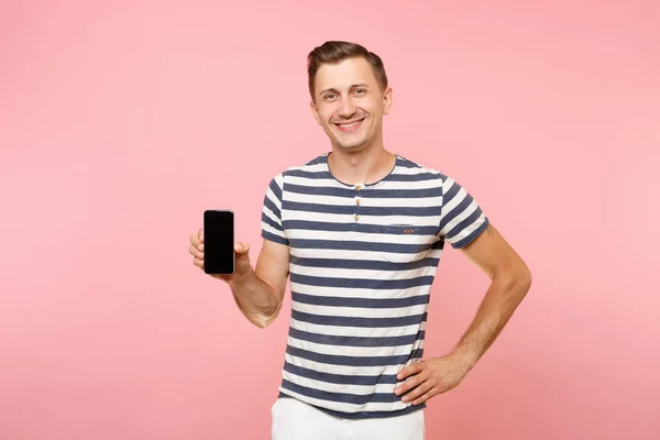 Portrait of man in striped t-shirt showing mobile phone camera with blank black empty screen copy space isolated on trending pastel pink background. People sincere emotions concept. Advertising area