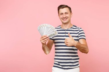 Gülümseyen portresi heyecanlı çizgili tişört holding pakette bulunan genç adam çok dolar, nakit para, şevk jest üstünde pembe arka plan izole kopya yer. İnsanlar samimi duygular yaşam tarzı kavramı