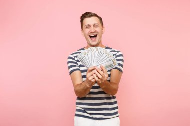 Gülümseyen portresi heyecanlı çizgili tişört holding pakette bulunan genç adam çok dolar, nakit para, şevk jest üstünde pembe arka plan izole kopya yer. İnsanlar samimi duygular yaşam tarzı kavramı