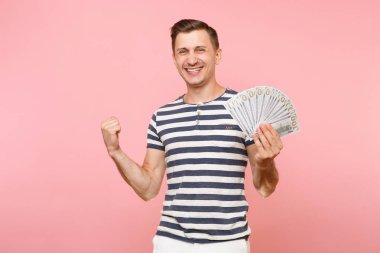 Gülümseyen portresi heyecanlı çizgili tişört holding pakette bulunan genç adam çok dolar, nakit para, şevk jest üstünde pembe arka plan izole kopya yer. İnsanlar samimi duygular yaşam tarzı kavramı