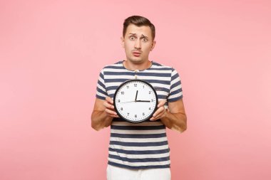Dikey şok üzgün üzgün giyen çizgili tişört yuvarlak saat tutan adam, pastel pembe arka plan eğilimleri izole alanı kopyalayın. İnsanlar samimi duygular yaşam tarzı kavramı. Zaman azalıyor
