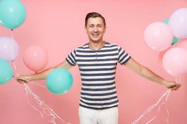 Parlak pembe eğilimleri arka plan üzerinde izole renkli hava balonları tutan çizgili tişört giyen büyüleyici genç mutlu bir adam portresi. İnsanlar samimi duygular yaşam tarzı kavramı. Reklam alanı