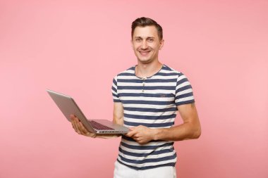 Dizüstü bilgisayar, eğilimleri pastel pembe arka plan üzerinde izole kopya alanı üzerinde tişört giyen yakışıklı genç adam portresi çizgili. İnsanlar samimi duygular yaşam tarzı kavramı. Reklam alanı