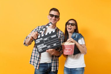 Genç gülen kaç kadın adam 3d gözlük Klaket kova patlamış mısır yapım klasik kara film tutan tarihte film film izlerken sarı arka plan üzerinde izole. Sinema kavramı duygular