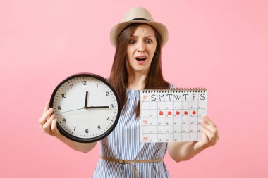 Yuvarlak saat, pembe eğilimleri arka plan üzerinde izole adet gün kontrol etmek için dönemleri takvim tutan mavi elbiseli şok karışık üzgün kadın. Tıbbi jinekolojik kavramı. Kopya alanı