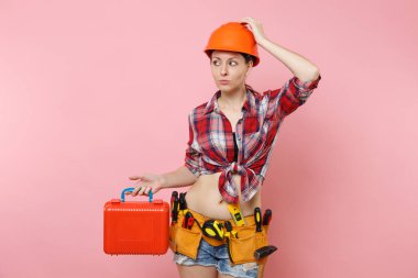 Güçlü genç tamirci kadın portakal kask, ekose gömlek, kot şort, aletleri, dolu, pembe arka plan izole araç seti araçları kemer. Kadın erkek iş. Yenileme işgal kavramı