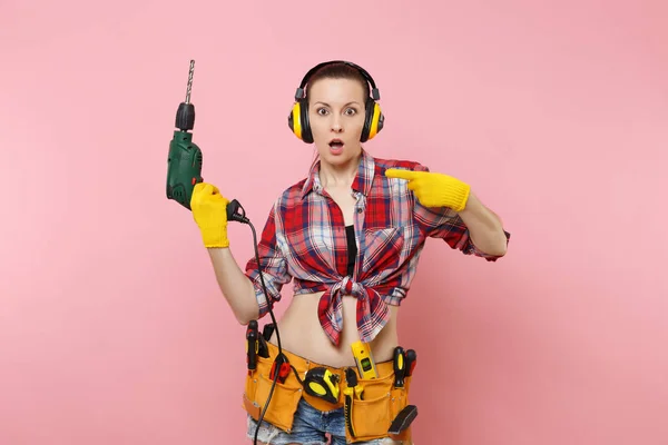 能量性感的杂女在手套 隔音耳机 套件工具带充满电力电钻在粉红色背景隔离的仪器 女性在男性工作 装修理念 — 图库照片